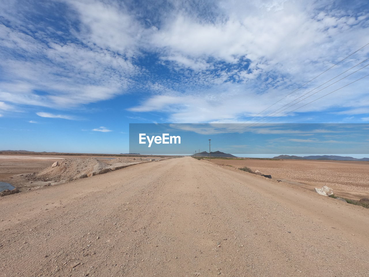 DIRT ROAD ON DESERT LAND AGAINST SKY