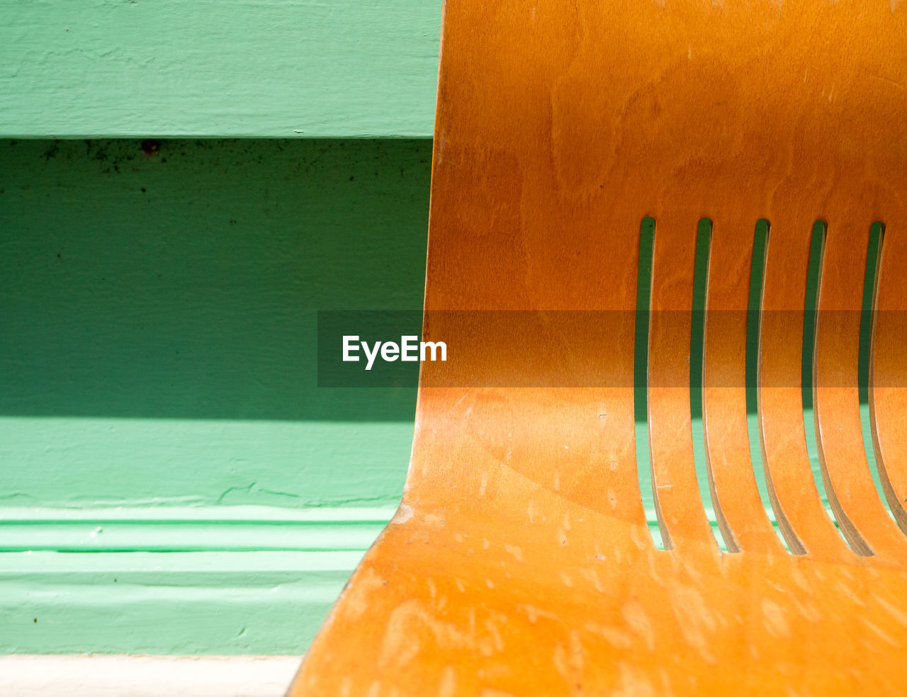 Colour close up of a curved wooden chair with cut out lines, against a green wall