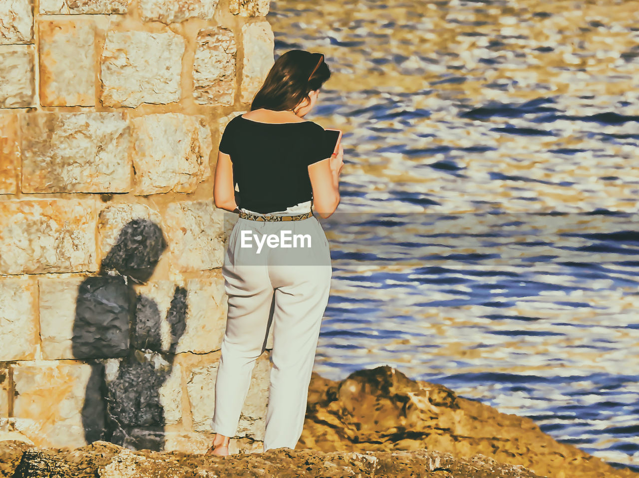 REAR VIEW OF WOMAN STANDING BY WALL