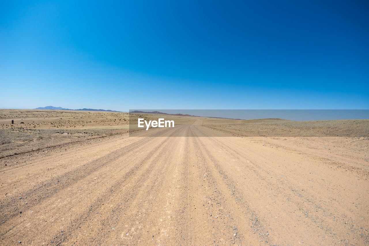 Tire tracks on desert against clear blue sky