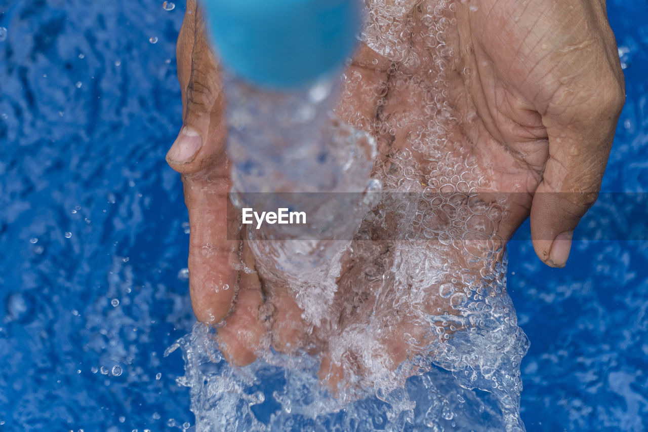 Water splashing on cropped hands at swimming pool