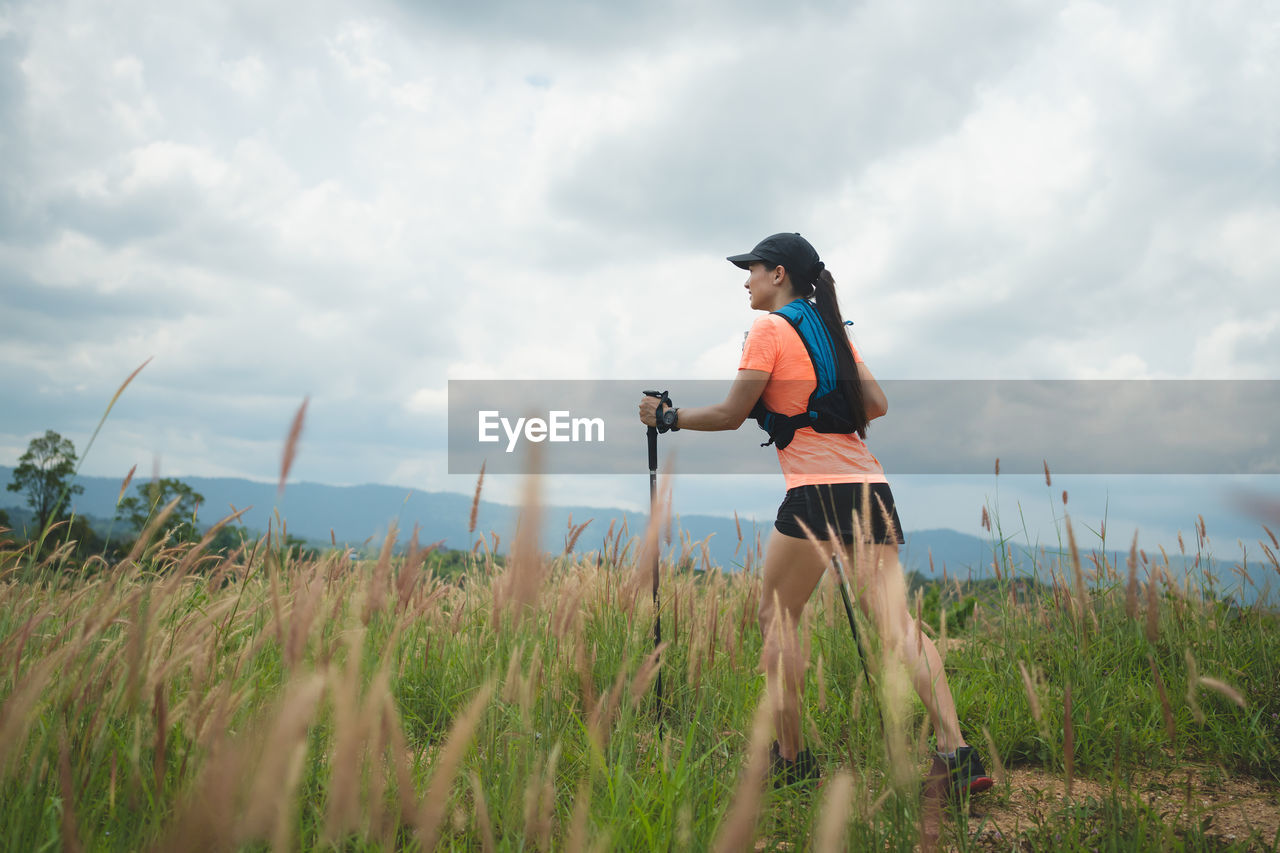 rear view of woman with arms outstretched standing on field against sky