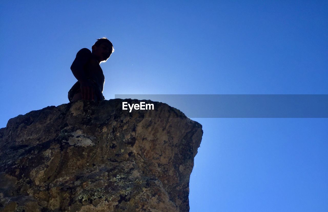 Low angle view of man on rock against blue sky