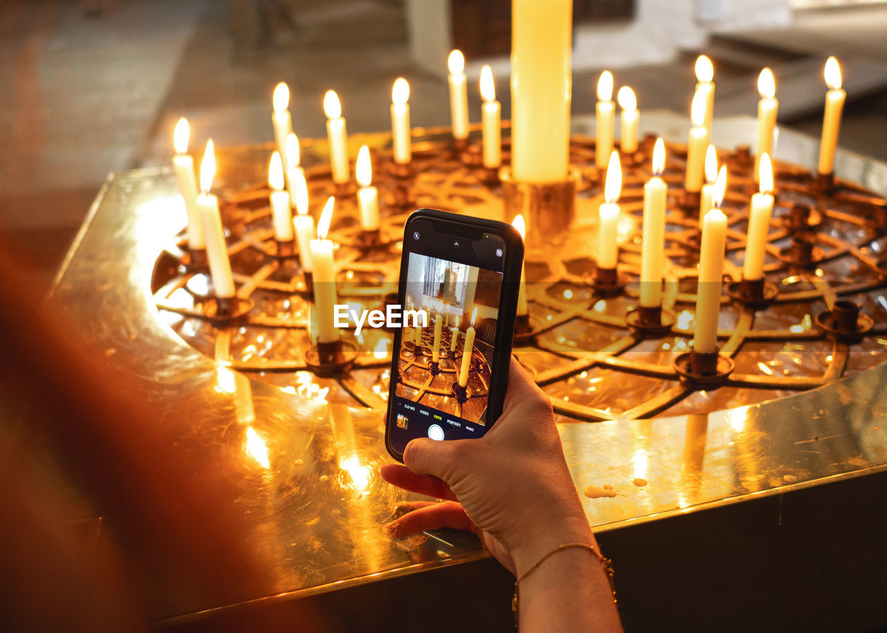 cropped hand holding illuminated tea light candles on table