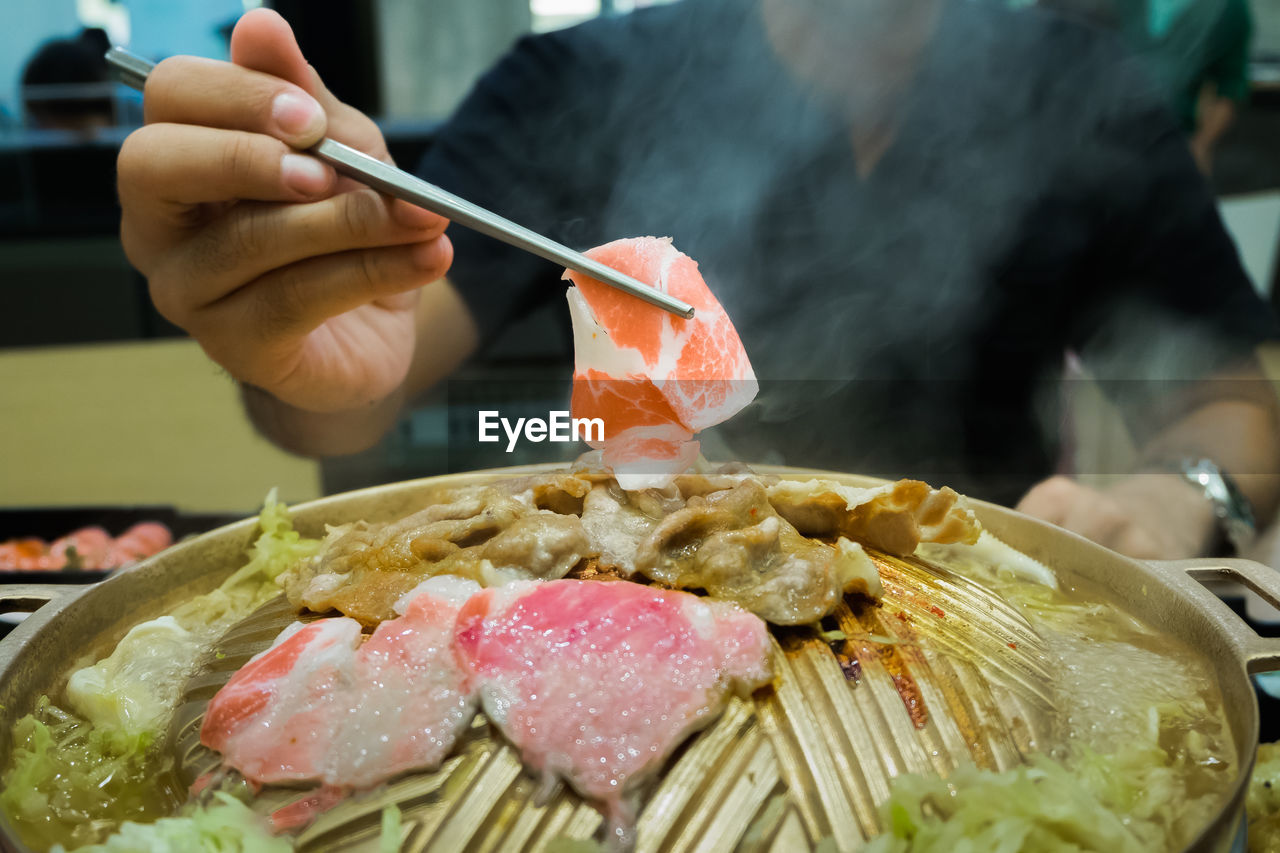 Midsection of man holding meat with chopsticks at restaurant