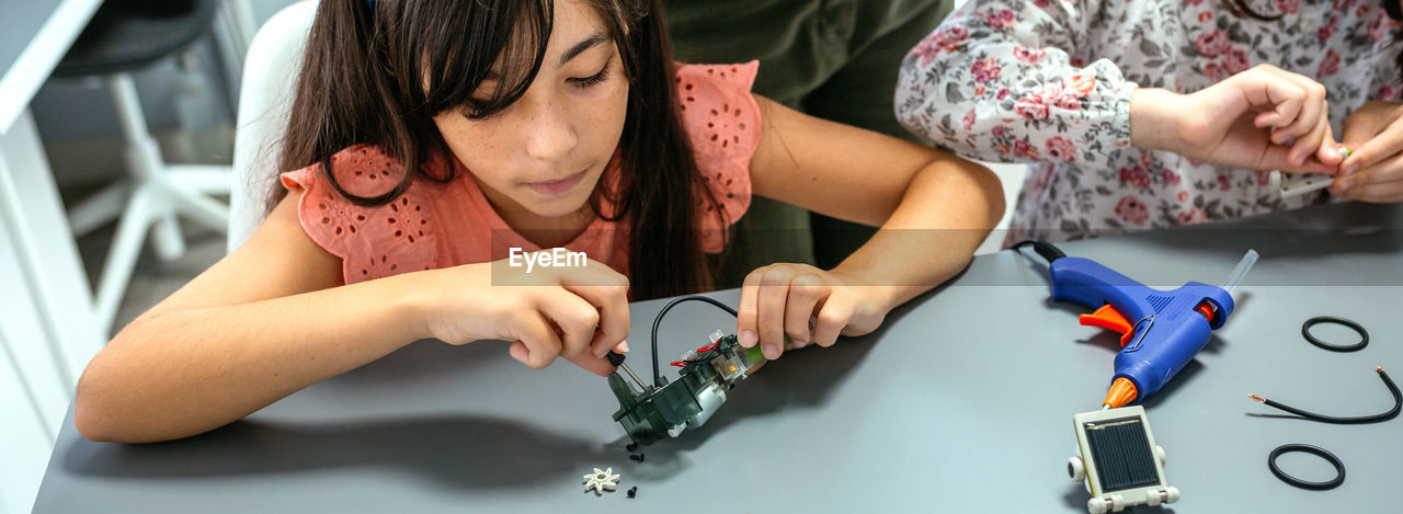 Student screwing electrical circuit next to schoolchild in robotics class