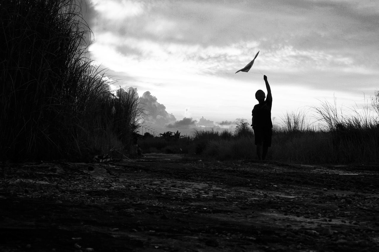 Silhouette boy flying kite on field against sky