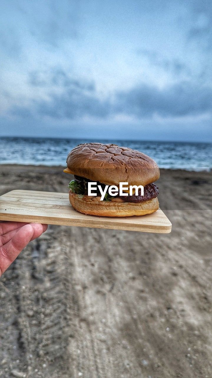 A hamburger on a wooden tablet by the ocean 