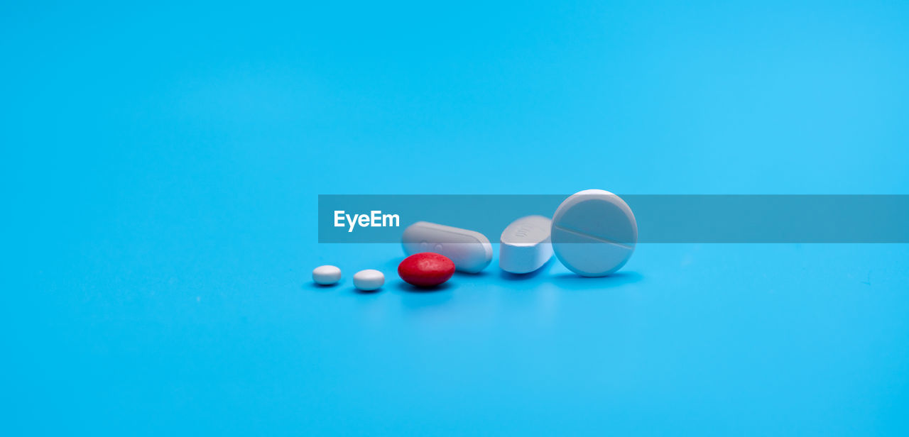 Group of round and oval white tablets pills, red sugar-coated tablets pills on blue background. 