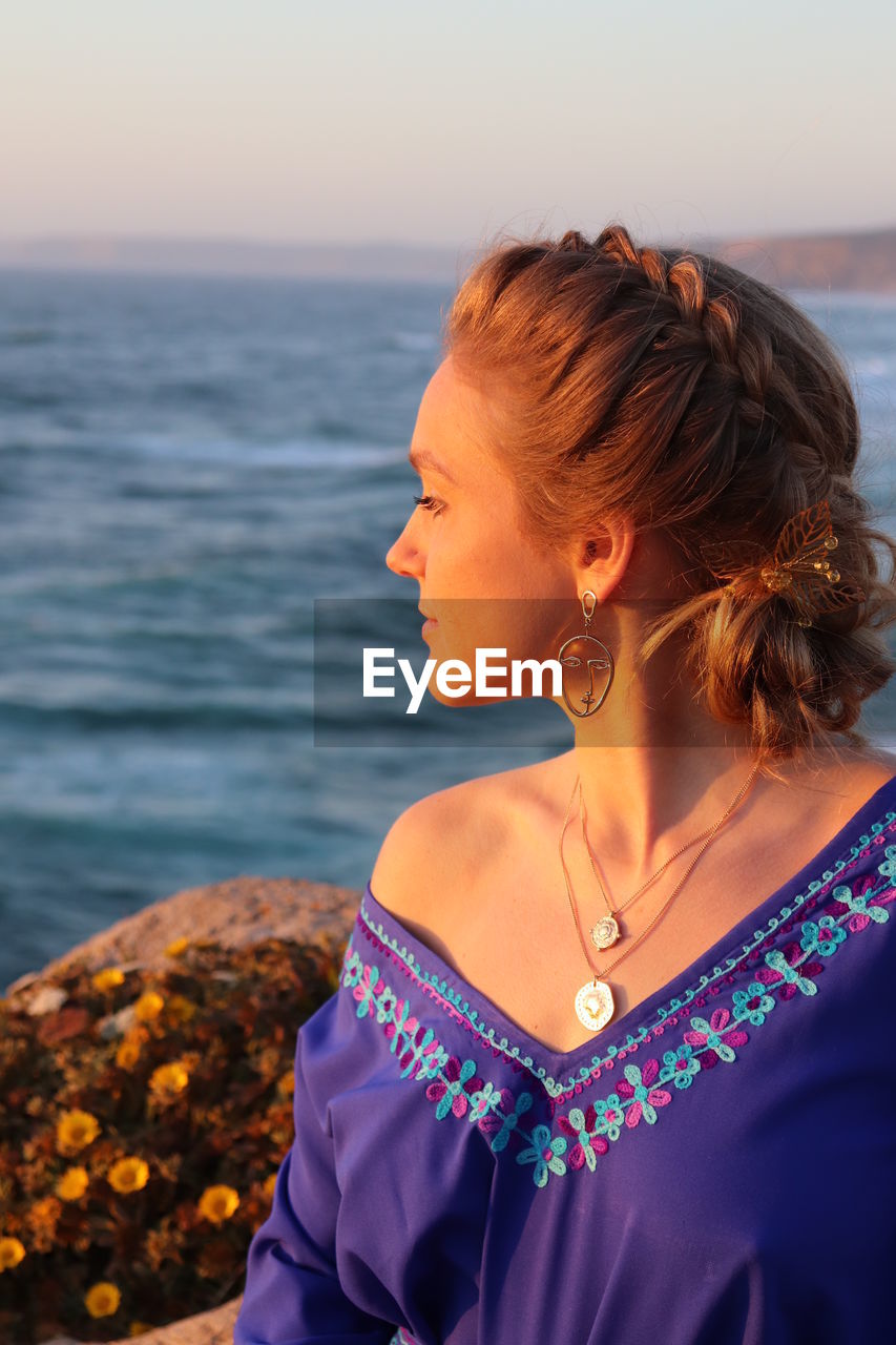 Midsection of woman by sea against sky during sunset