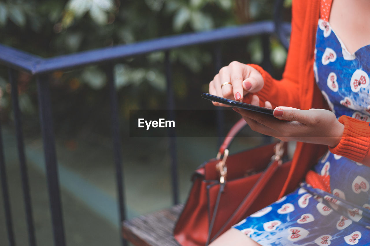 Midsection of woman using mobile phone on bench 