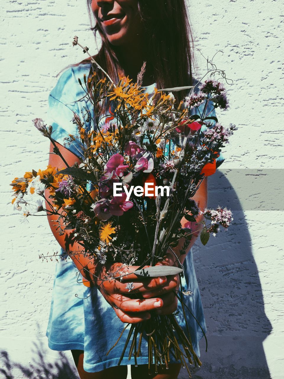 Midsection of woman holding bouquet while standing by wall