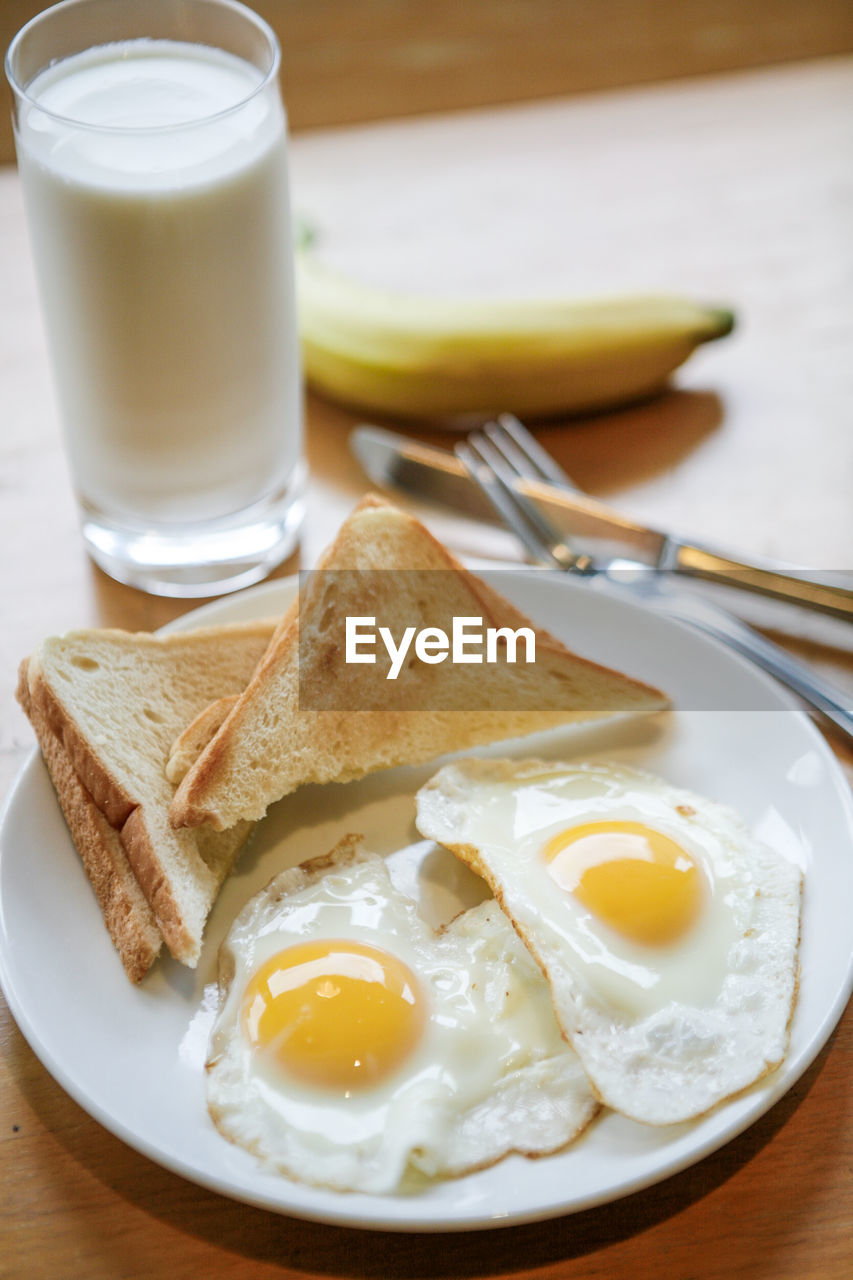 Close-up of fried eggs and breads in plate by milk glass on table