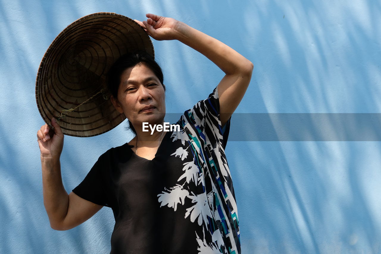 Mature woman wearing asian style conical hat against wall