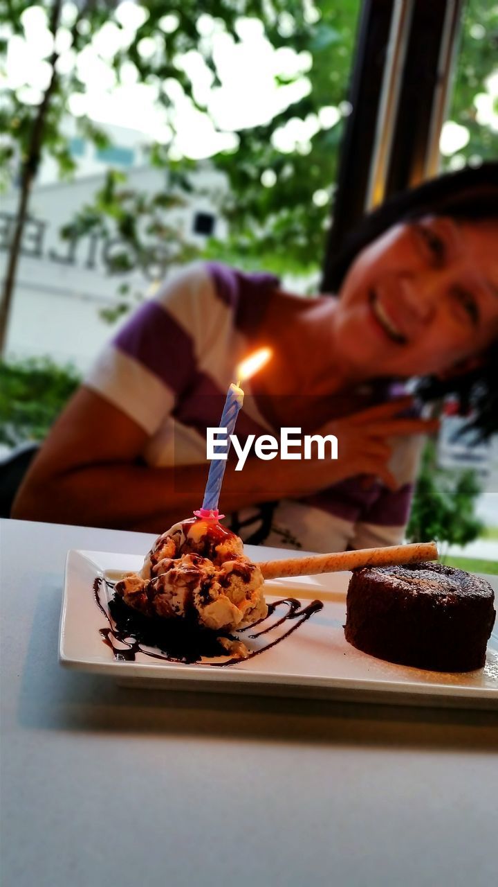 Lit candle on birthday cake against mature woman