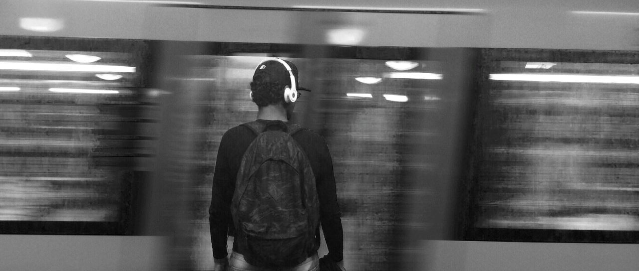 Rear view of man with headphones against blurred motion train at station