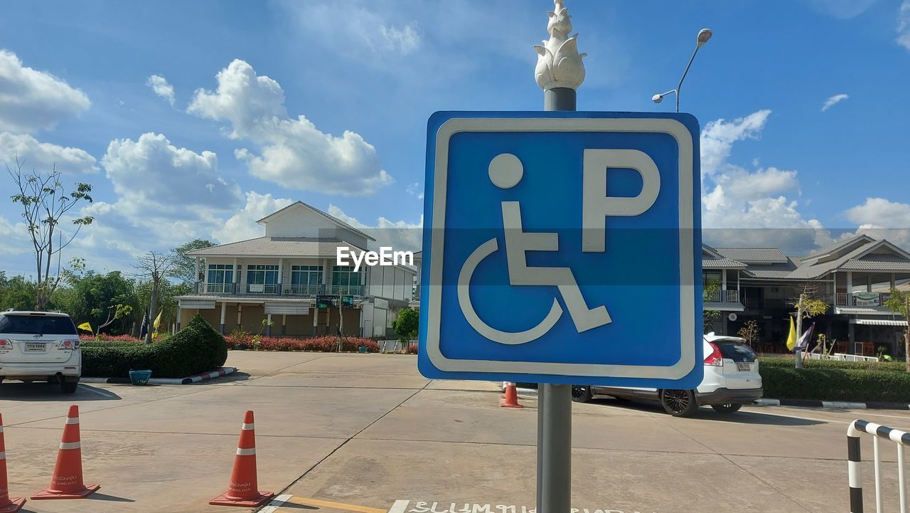 cloud, sign, architecture, sky, road, road sign, transportation, communication, building exterior, city, built structure, car, motor vehicle, mode of transportation, nature, street, traffic sign, day, signage, guidance, no people, blue, building, text, outdoors, disabled access, vehicle, disabled sign, information sign, travel, symbol