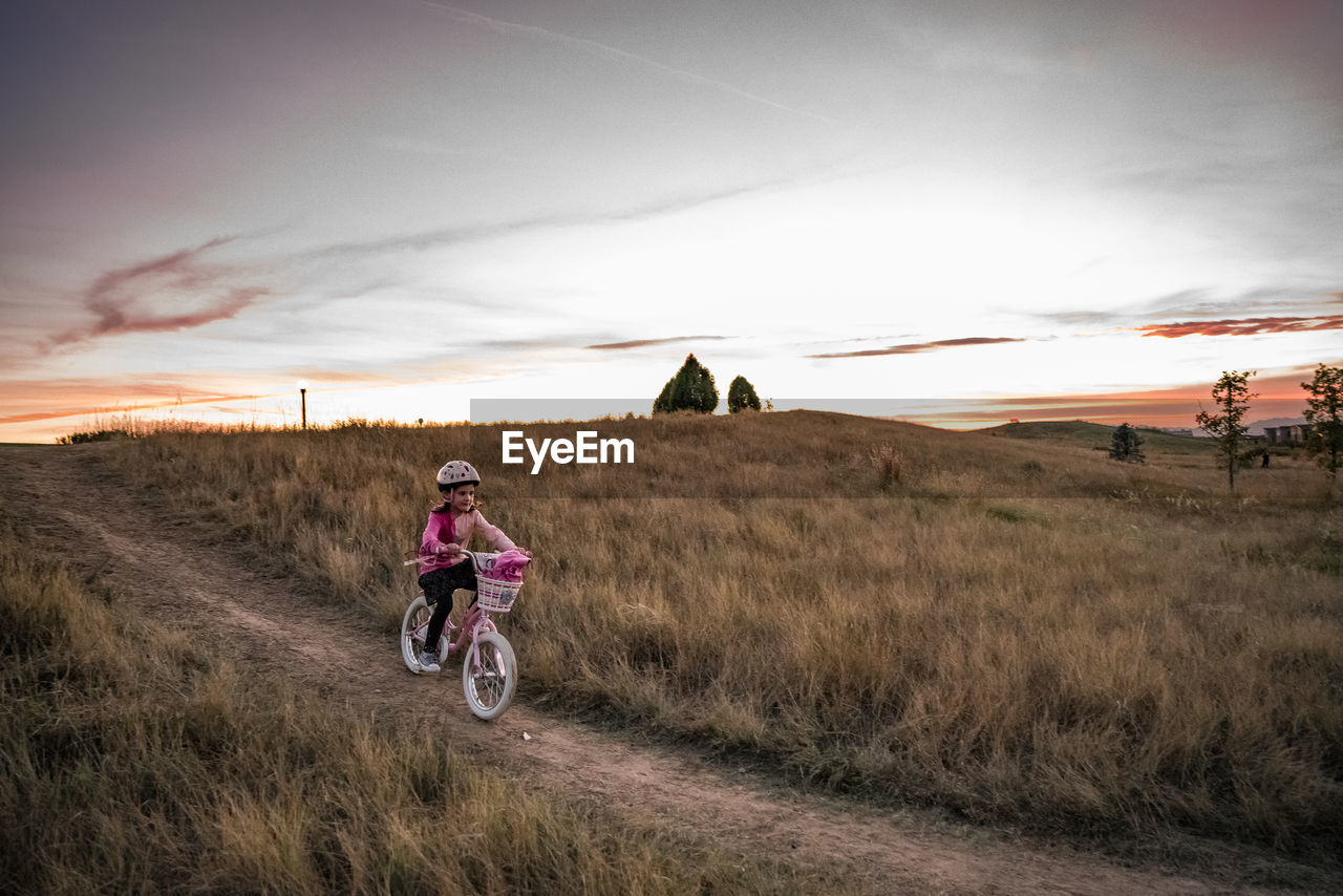 Young girl bikes down a grassy hill at sunset