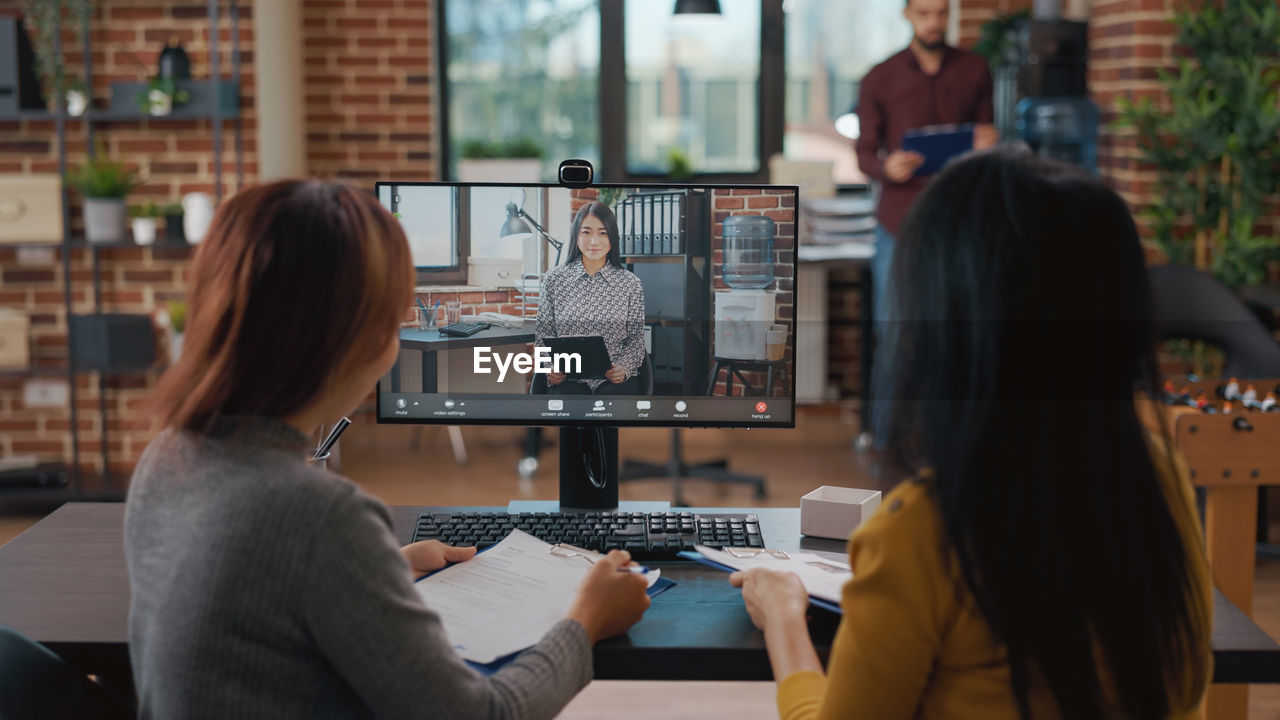 Rear view of businesswomen talking on video call at office