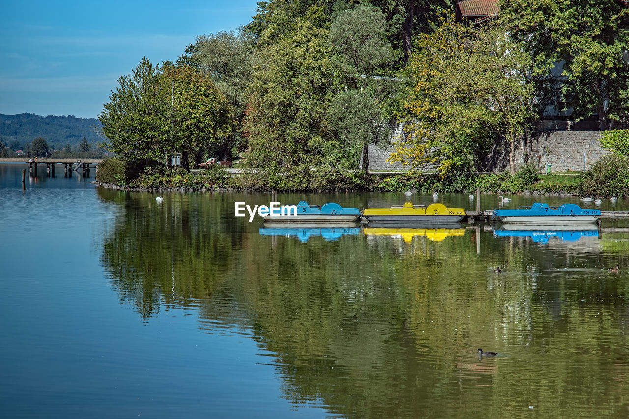 water, tree, reflection, plant, river, nautical vessel, nature, transportation, body of water, mode of transportation, day, vehicle, beauty in nature, boat, boating, tranquility, sky, no people, outdoors, pond, reservoir, scenics - nature, waterfront, waterway, tranquil scene, moored, travel, green, watercraft, blue, travel destinations, architecture, pedal boat