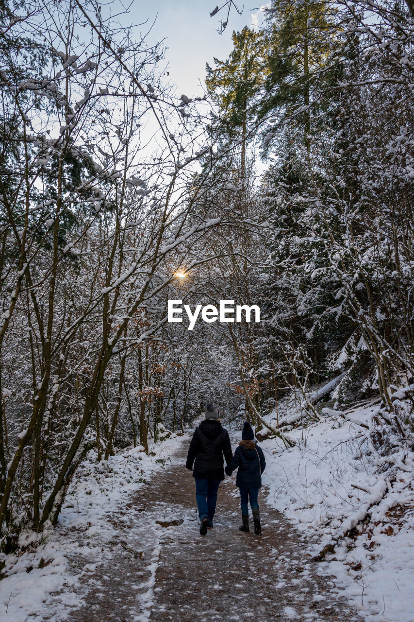 Rear view of mother and son walking on snow covered trail amidst trees