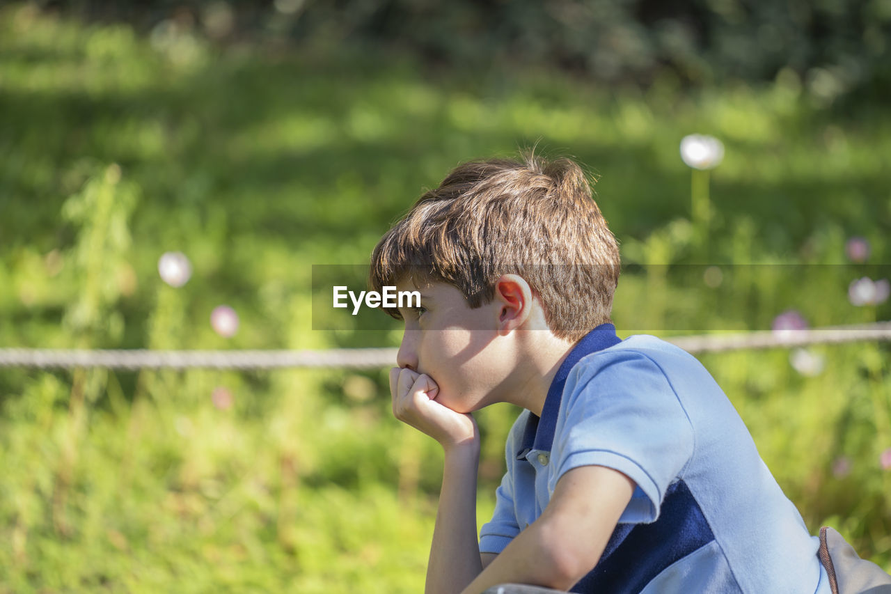 Upset little caucasian boy feels hurt sad bored thoughtful sitting alone in a park.