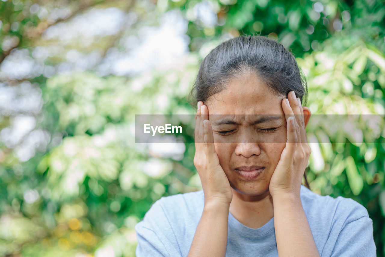 Woman touching head in pain against trees