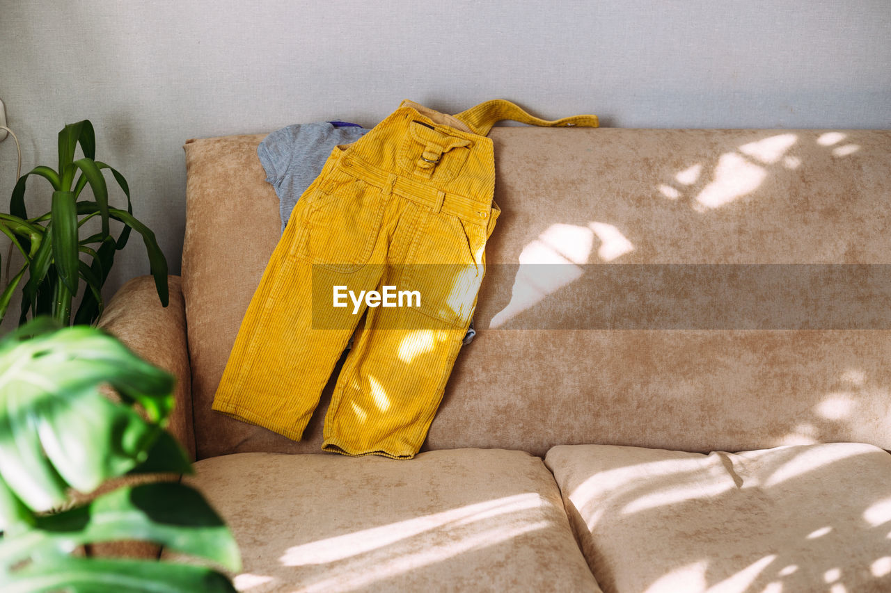 Children's clothing yellow jumpsuit and t-shirt lie on the sofa.