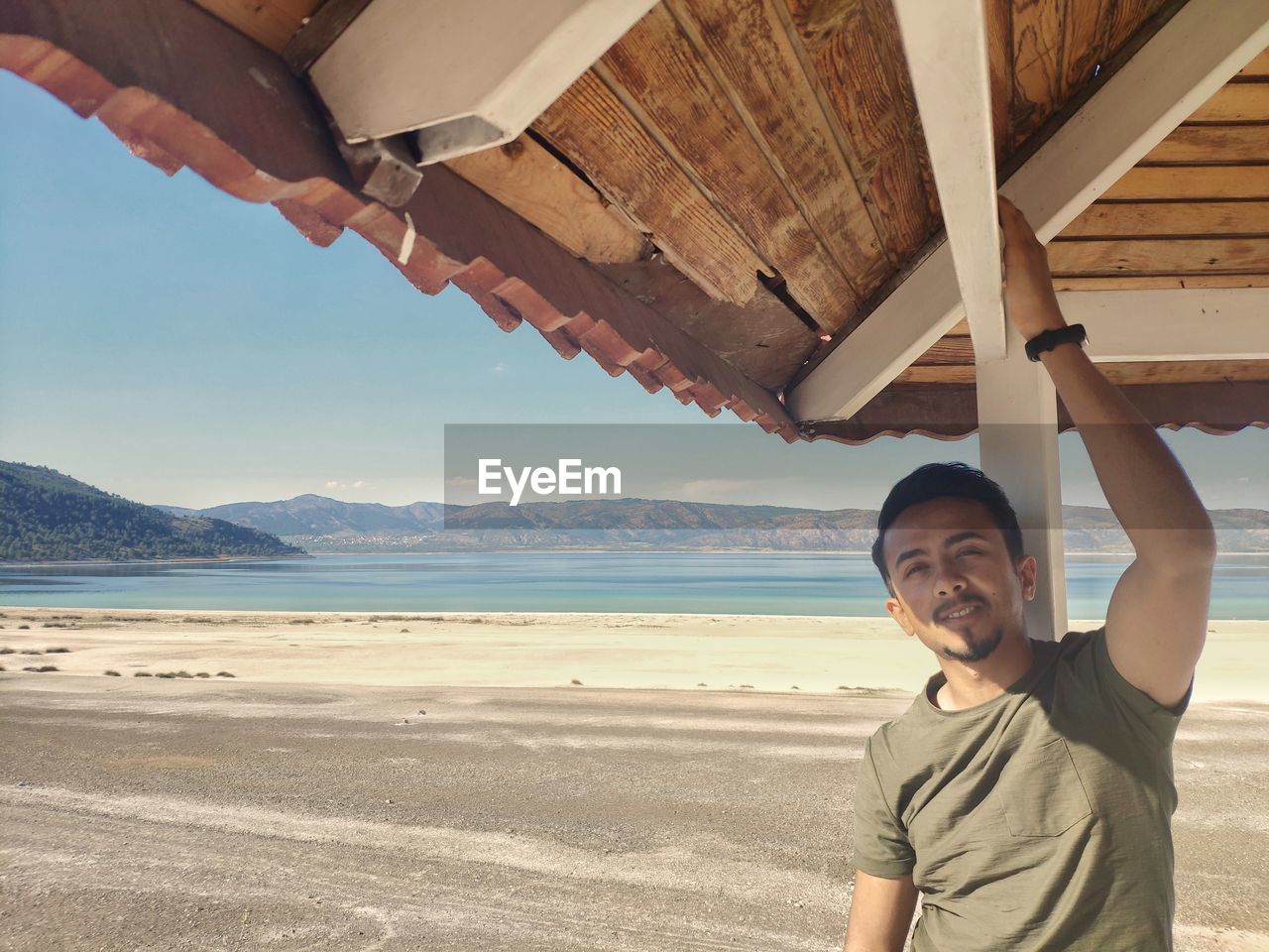 Portrait of man touching ceiling of gazebo at beach