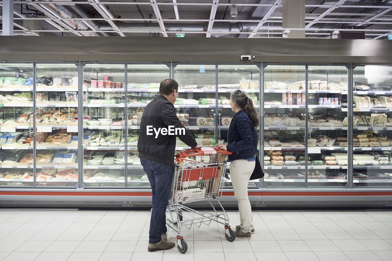 Mature couple looking at food on display at refrigerated section in supermarket