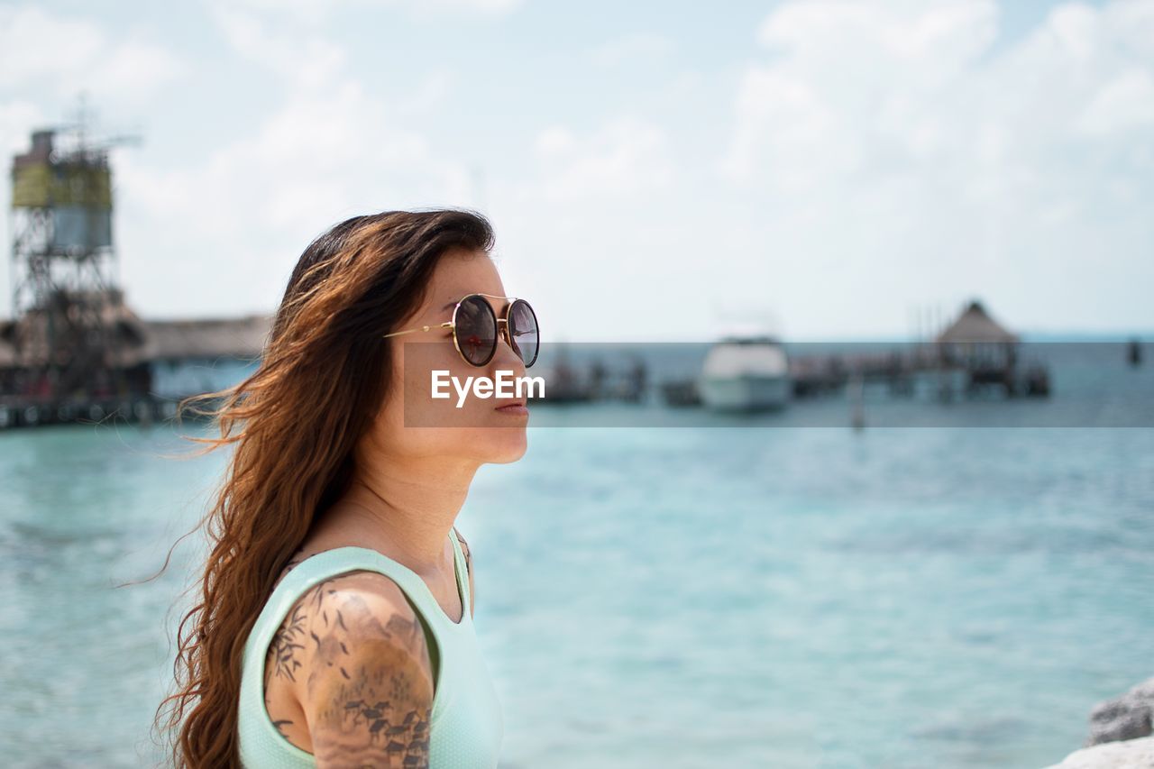 Young woman wearing sunglasses by sea against sky