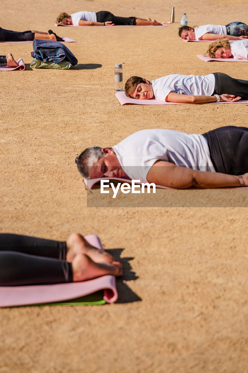Side view of calm women in activewear lying on mats on ground after yoga session in park in sunlight