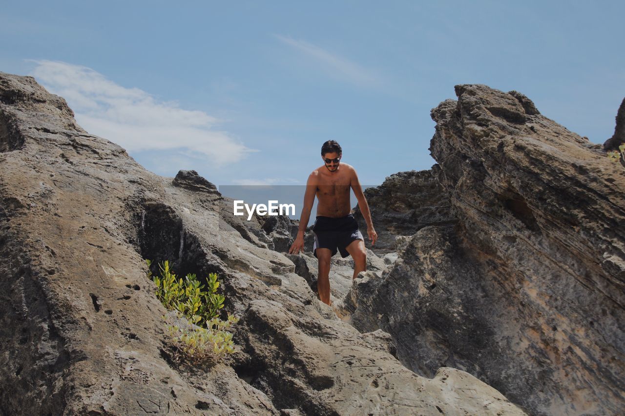 Low angle view of shirtless man standing on rock