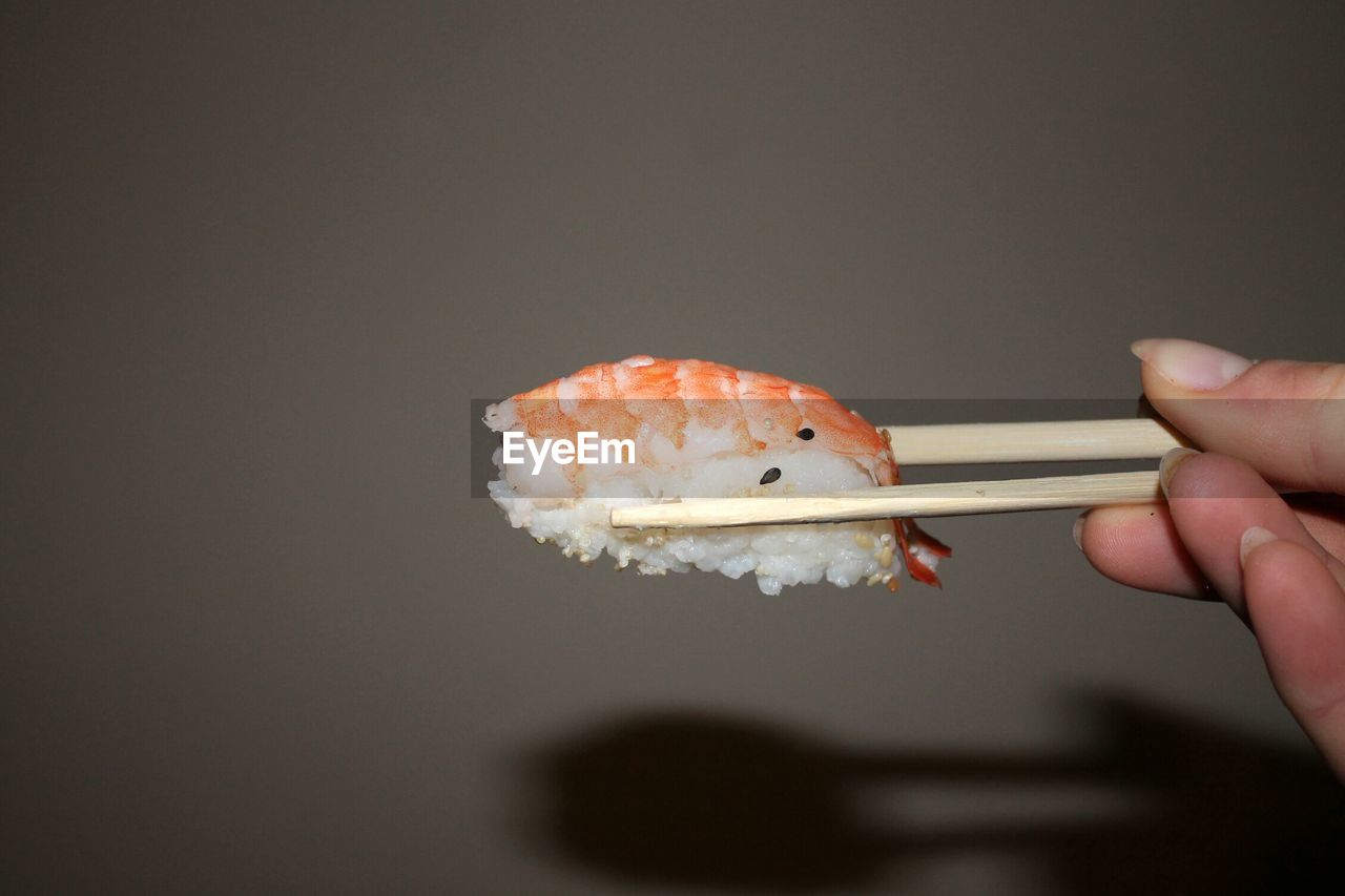 CLOSE-UP OF A HAND HOLDING SUSHI OVER WHITE BACKGROUND