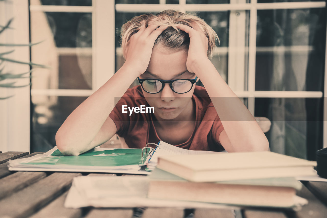 Frustrated boy siting next to books on desk at home