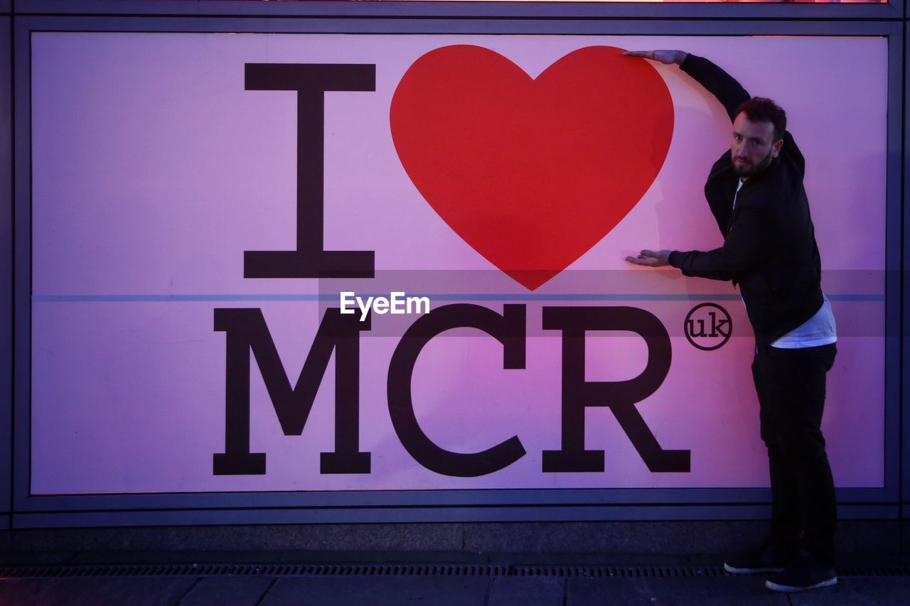 REFLECTION OF MAN AND WOMAN STANDING BY HEART SHAPE ON WALL