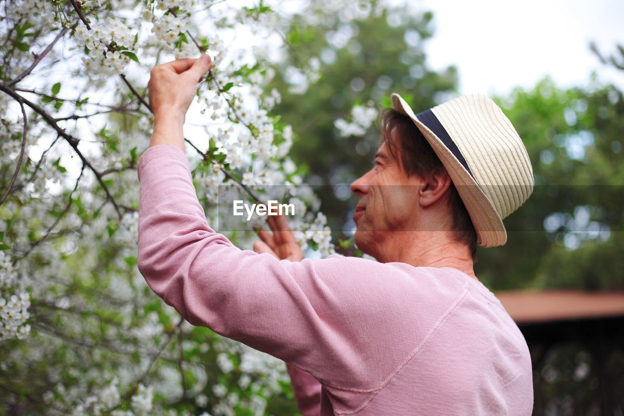 Side view of mature man picking flowers from plant