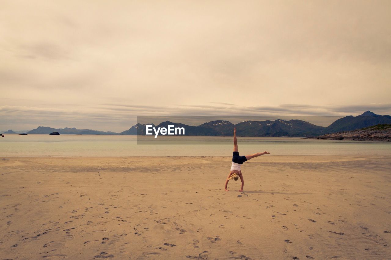 Woman doing handstand on shore at beach against sky