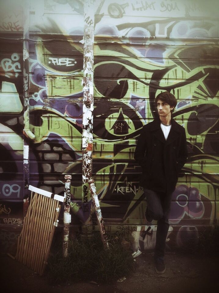Full length of serious man standing against graffiti wall