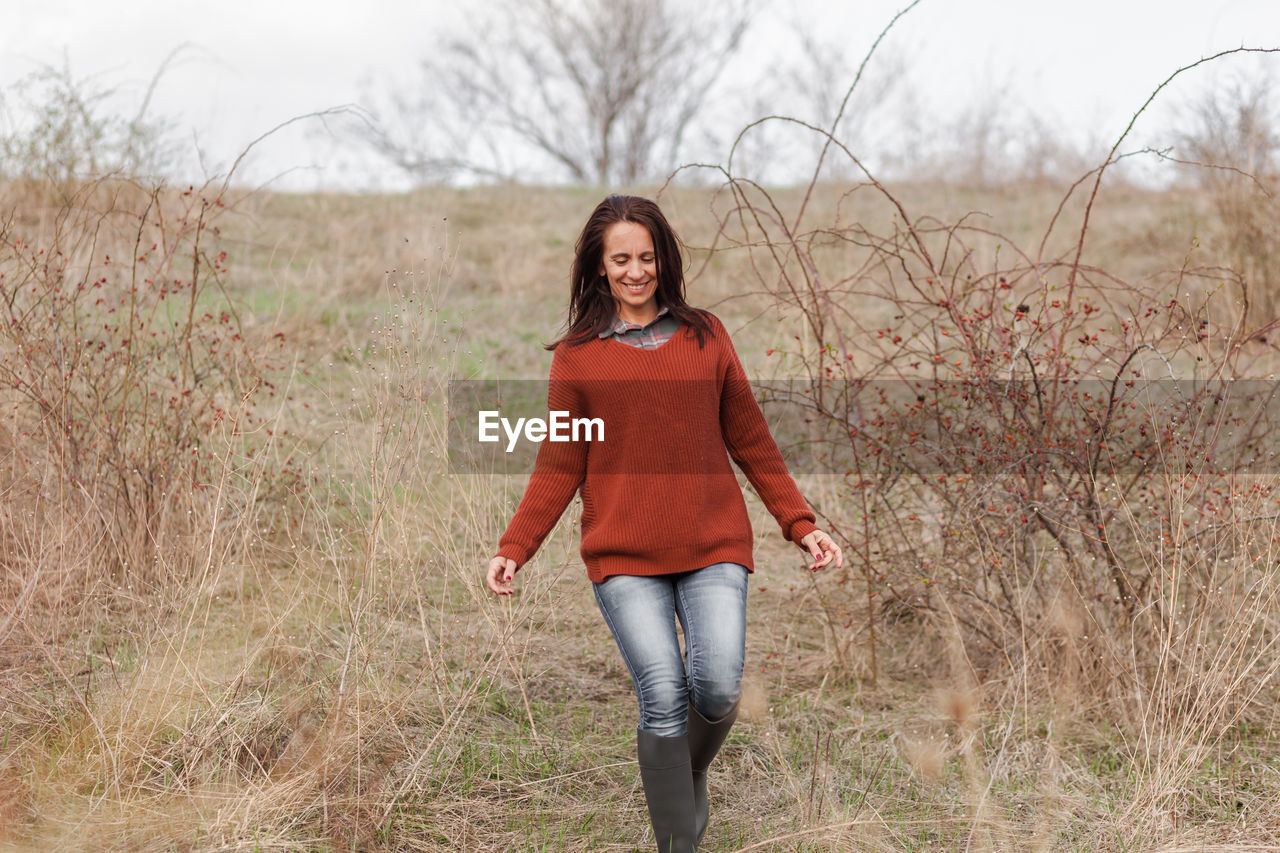 Smiling woman walking by plants against sky