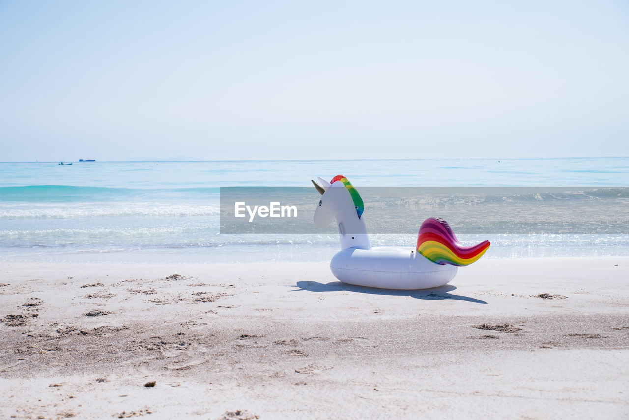 Unicorn shape inflatable ring at beach against sky