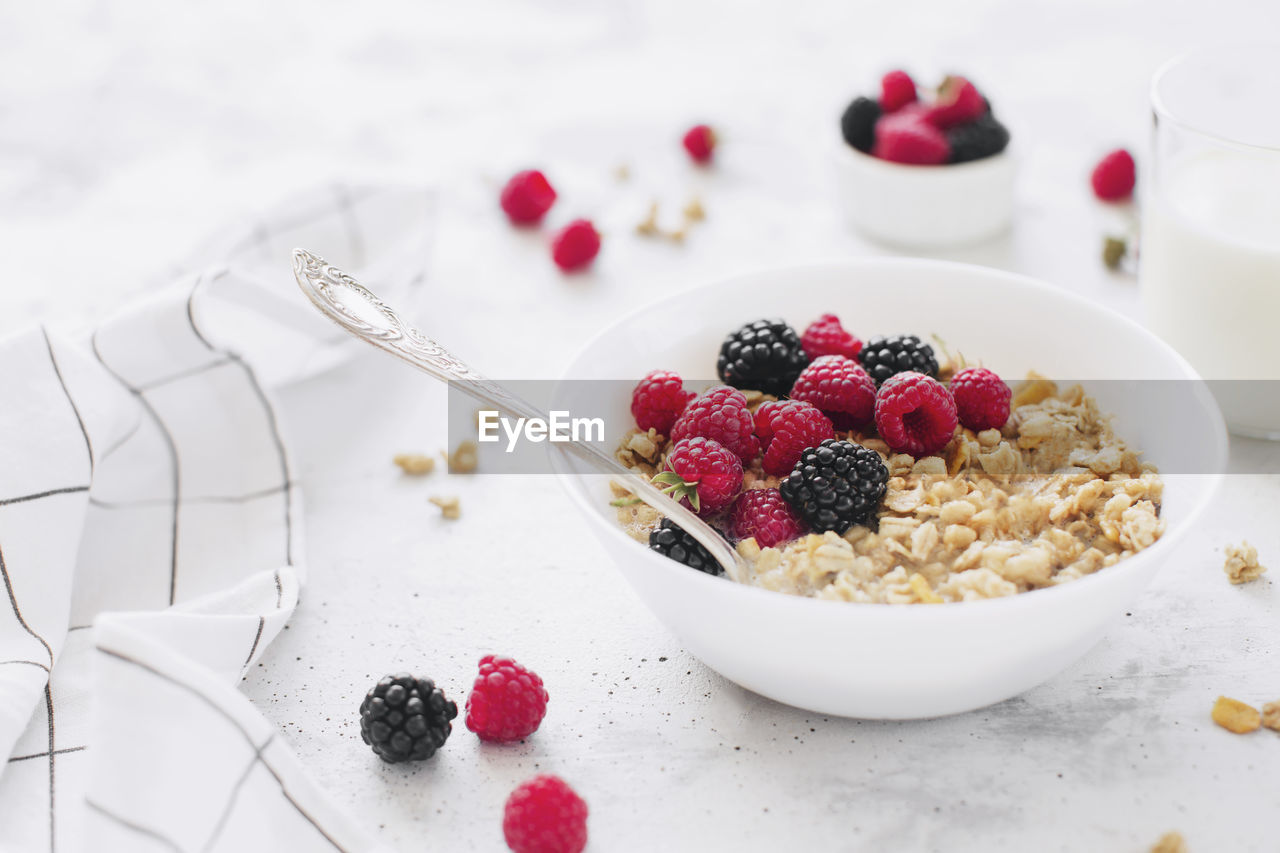 Morning healthy breakfast, white bowl full with granola, muesli, raspberry, blackberry on gray table