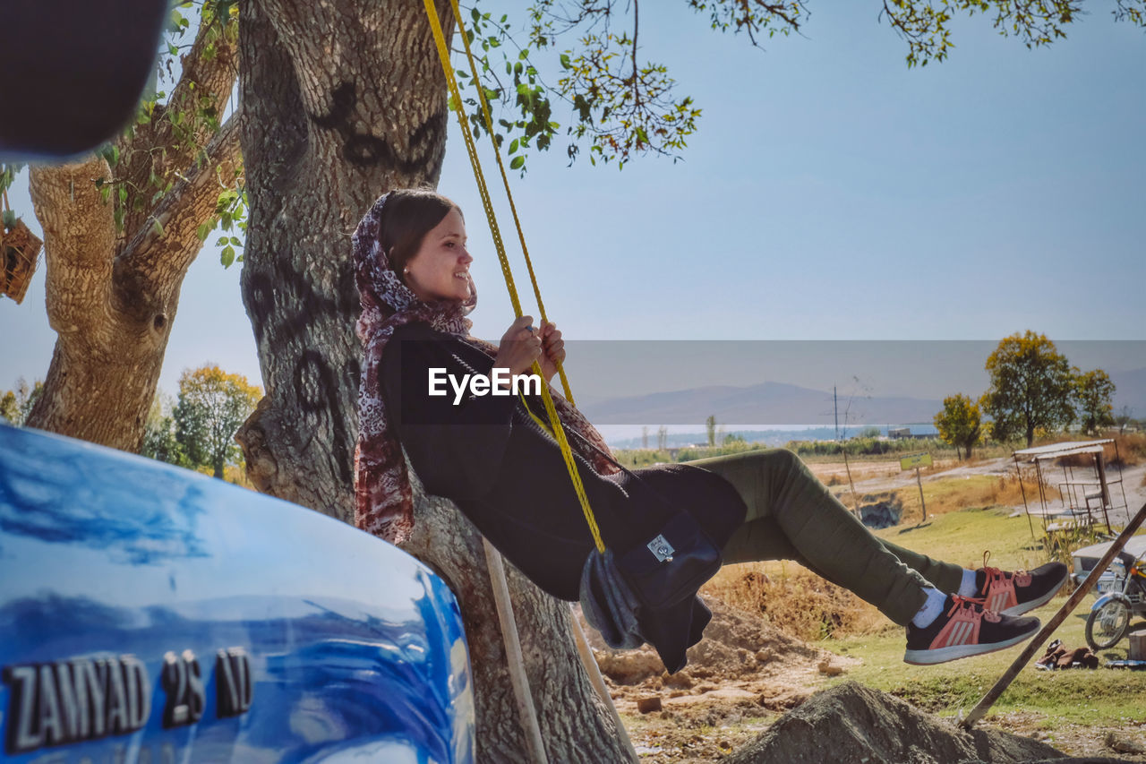 WOMAN SITTING ON TREE TRUNK