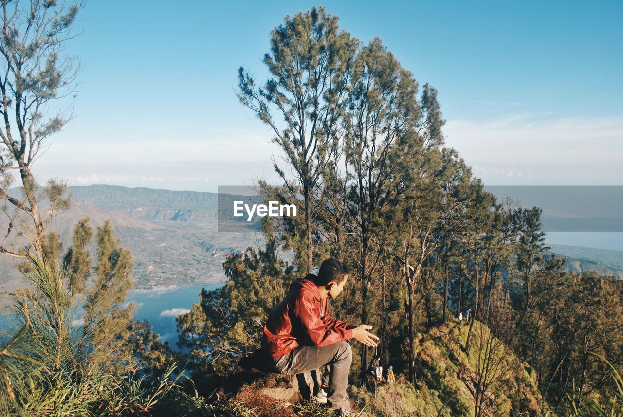 Man sitting on mountain against sky