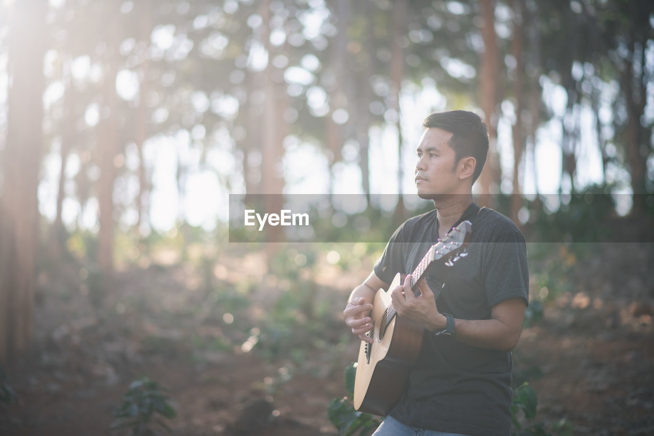 Young man using guitar while standing on land