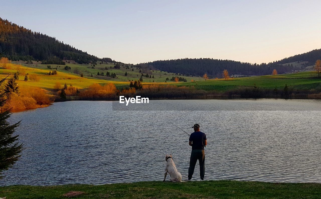 Rear view of man by dog fishing in lake