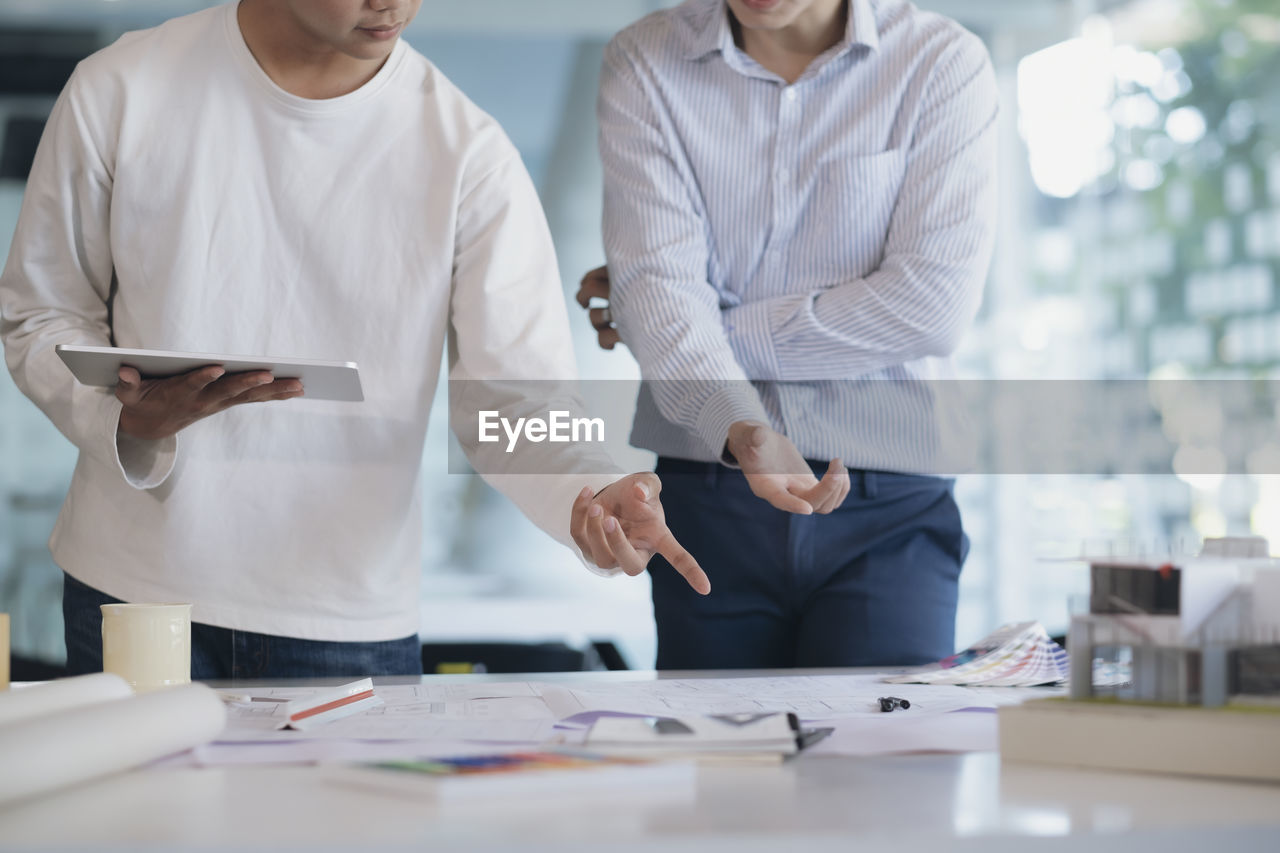 Midsection of colleagues discussing at desk in office