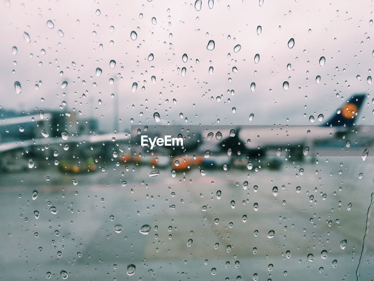 Airplane on airport runway seen through wet glass window during monsoon
