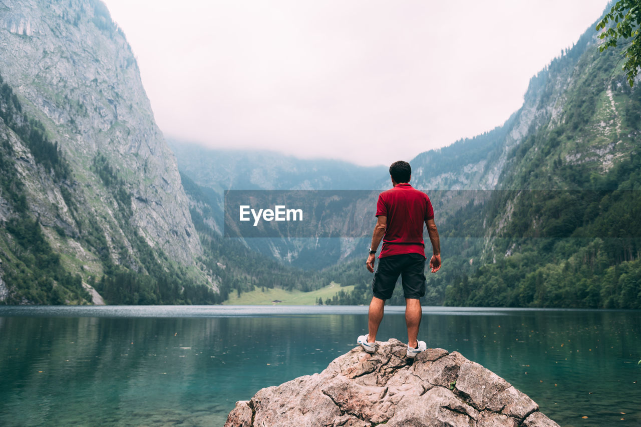 Rear view of man standing on rock by lake