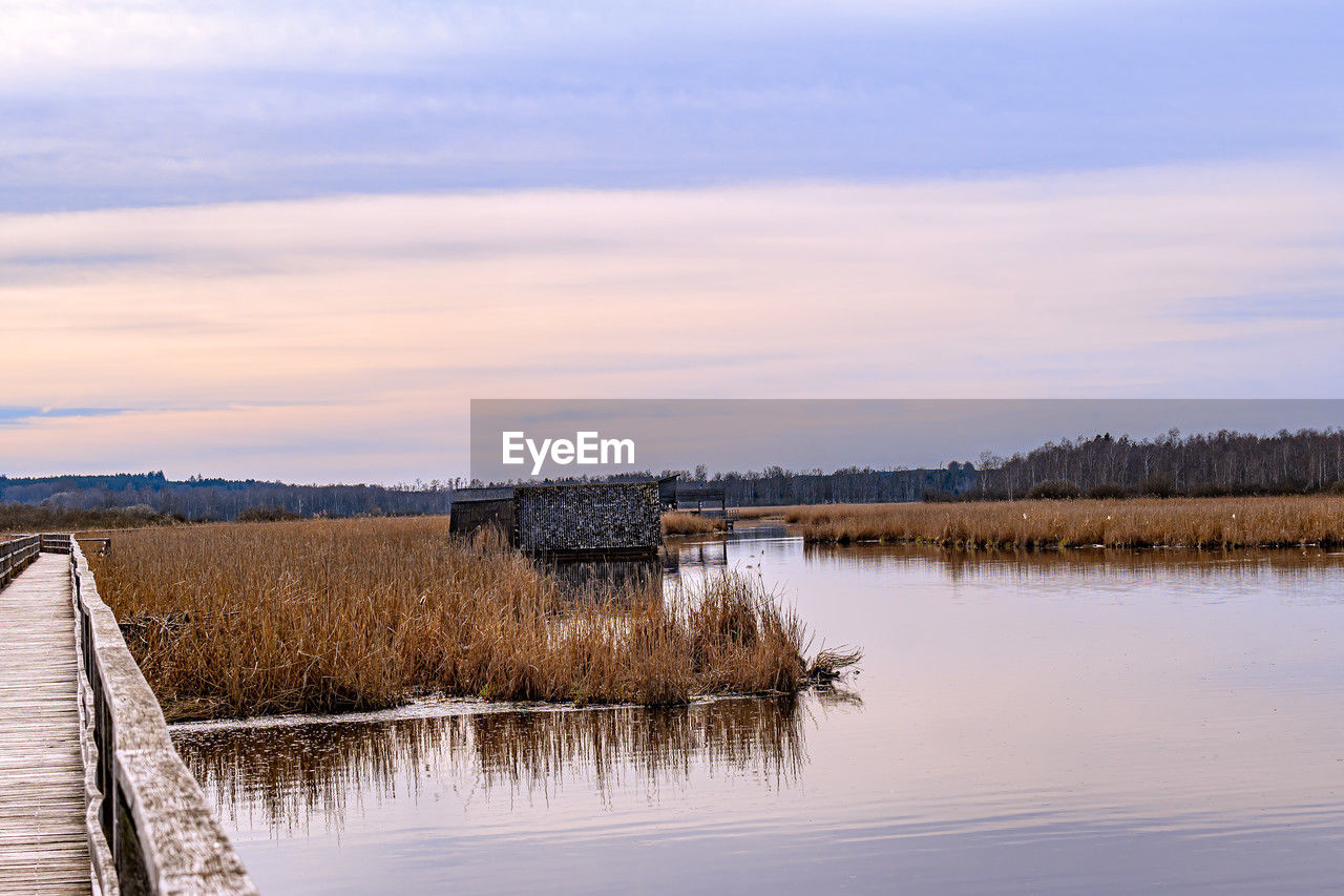 reflection, water, morning, sky, nature, shore, river, cloud, scenics - nature, reservoir, beauty in nature, winter, tranquility, environment, landscape, no people, marsh, tranquil scene, horizon, plant, tree, wetland, dawn, natural environment, architecture, land, outdoors, waterway, non-urban scene, rural scene, body of water, wood, day, travel destinations, built structure